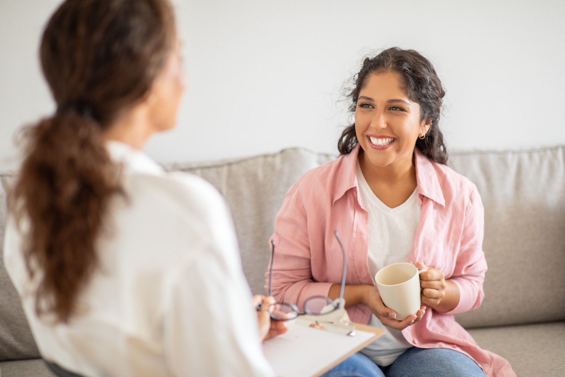 Woman in Pink Shirt Smiles While Sitting on a Couch